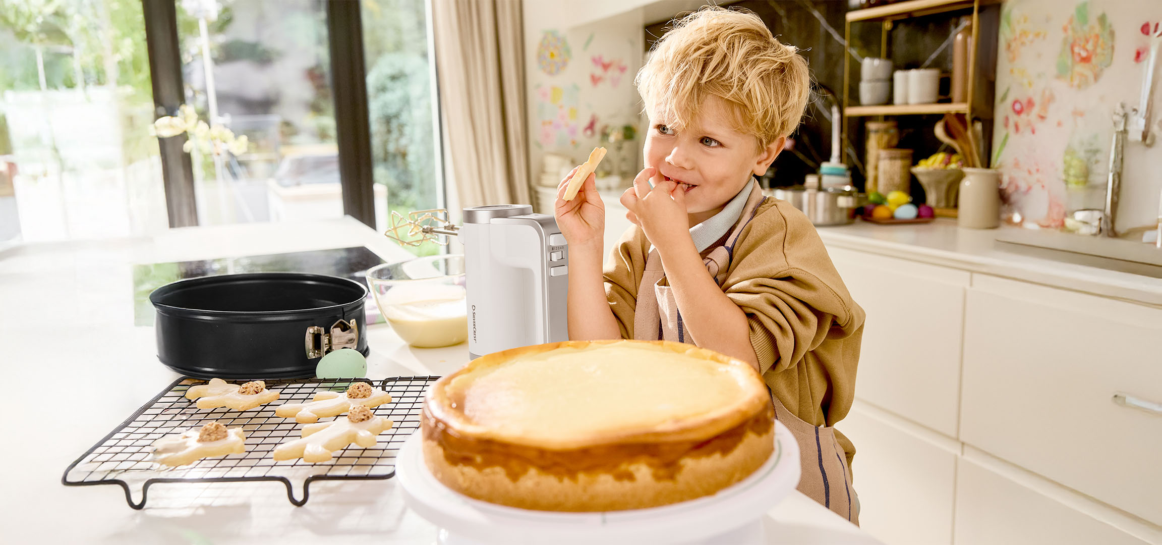 Boy tasting batter while baking a cake and cookies in the kitchen.