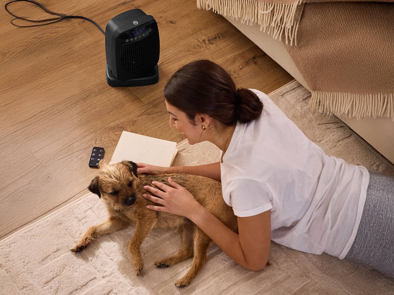 Woman petting a dog next to a black space heater on the floor.