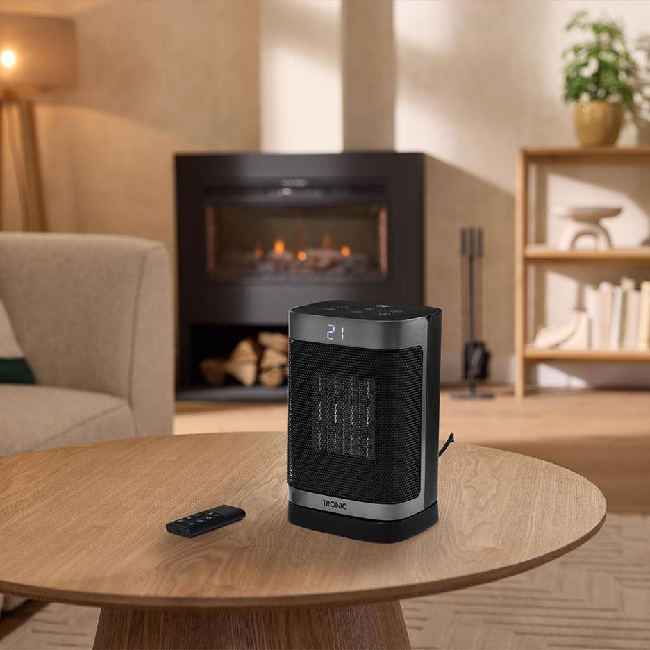 Portable ceramic heater with a remote control on a wooden table.