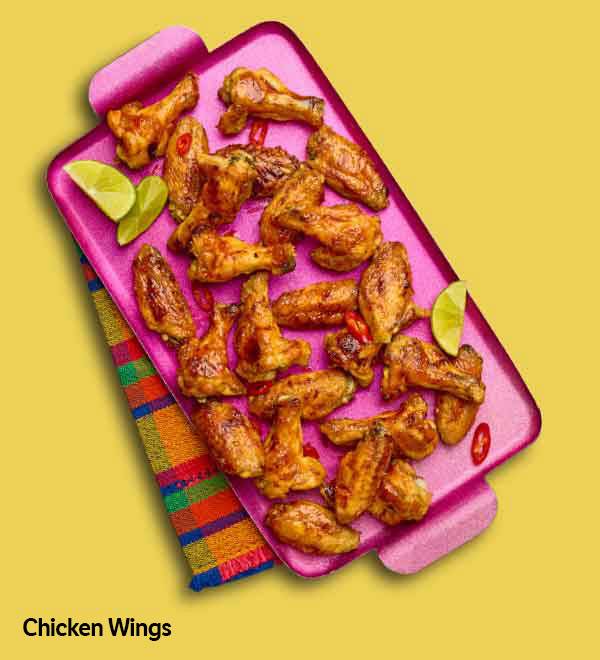 Spicy chicken wings on a pink tray with lime wedges.