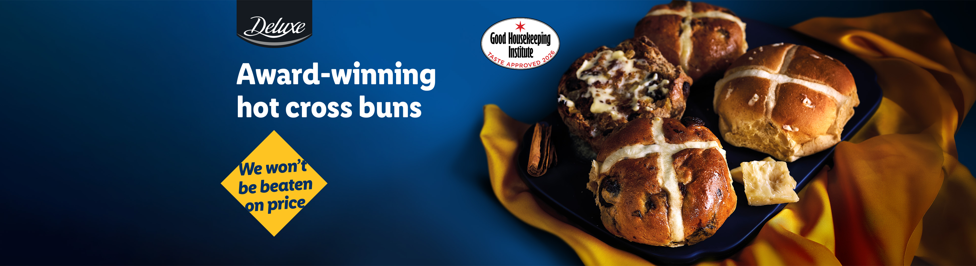 Award-winning hot cross buns, one with butter, on a blue plate with a yellow cloth.