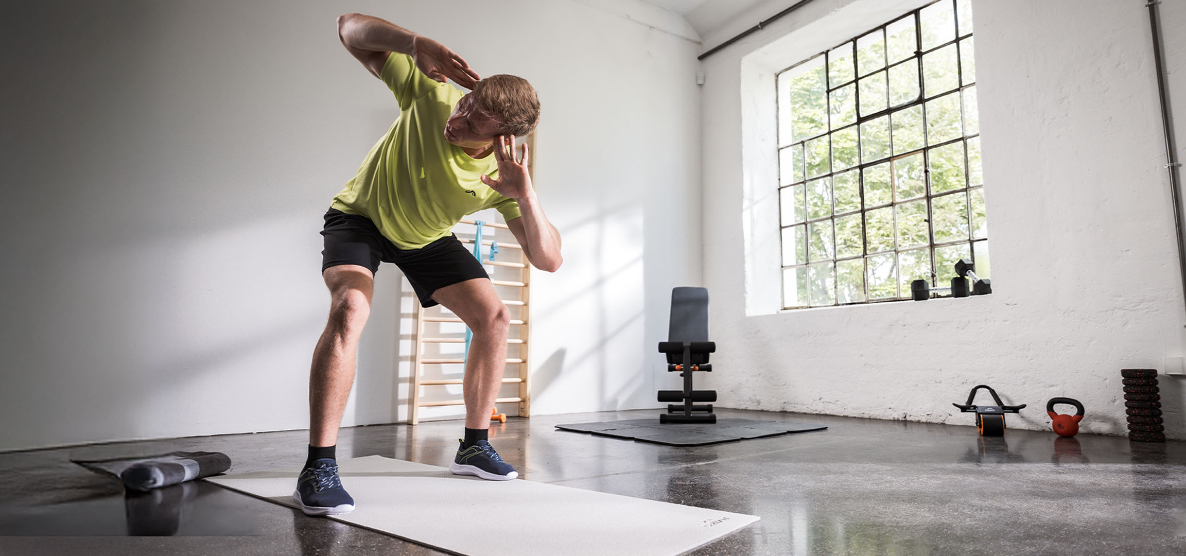 Man exercising in a gym, using a yoga mat and dumbbells.