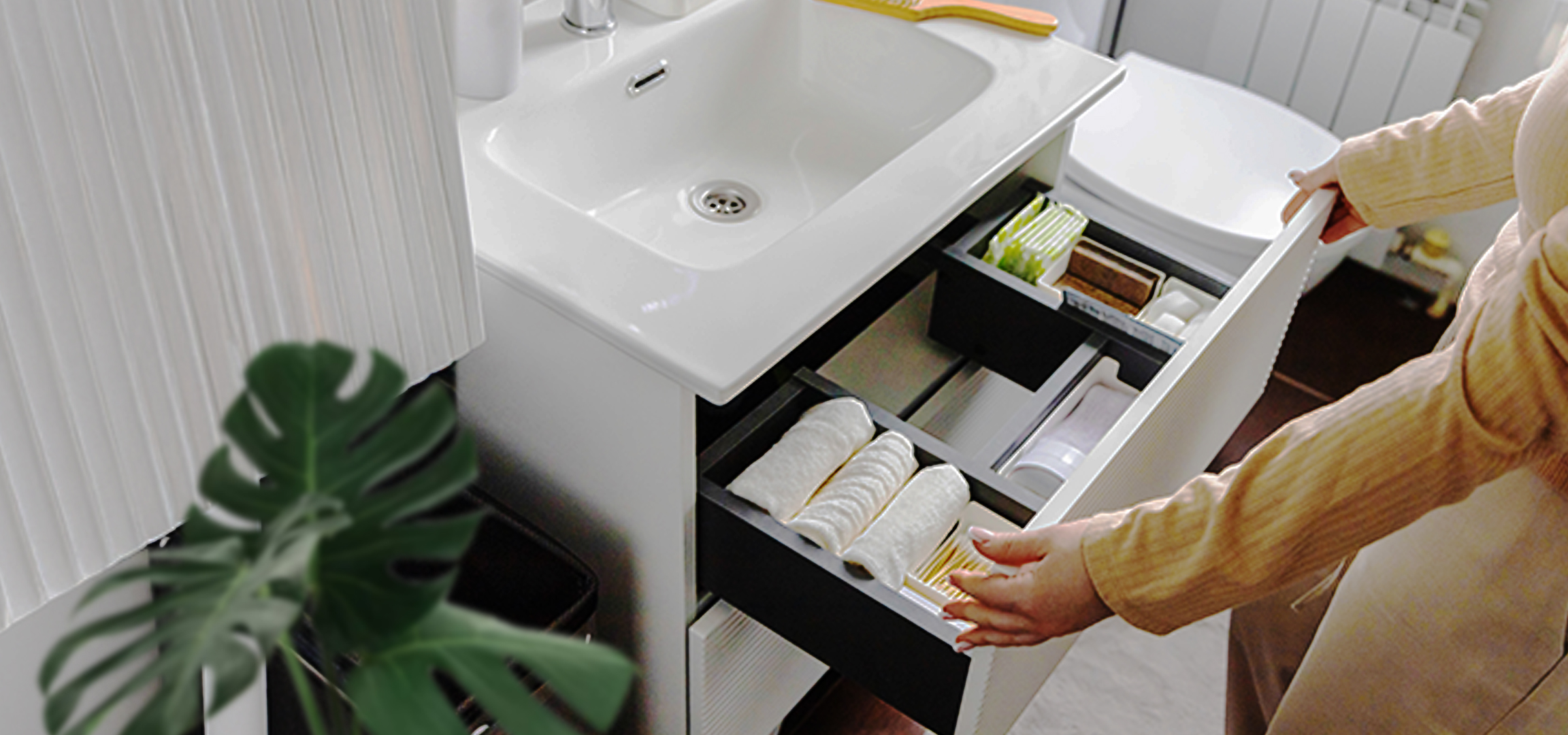 Woman organizing bathroom vanity drawer with towels, soaps, and hygiene products.