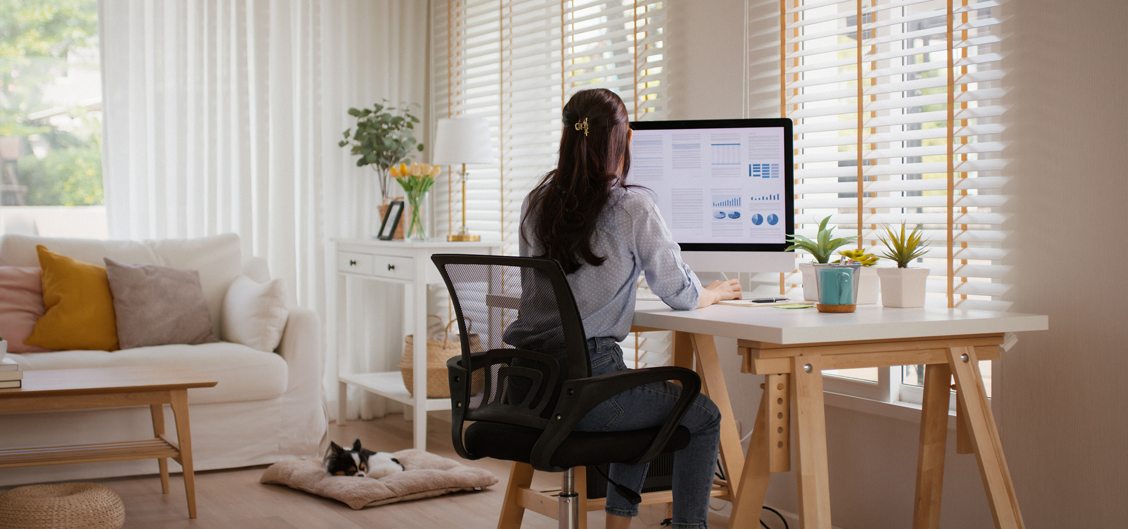 Woman working on computer in home office, dog sleeping on floor.