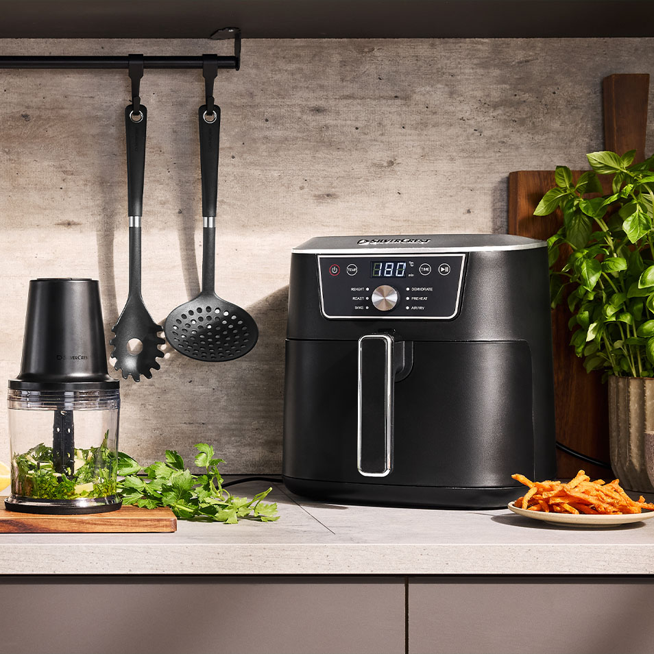 SilverCrest air fryer and food chopper on a kitchen counter with fresh herbs and sweet potato fries.