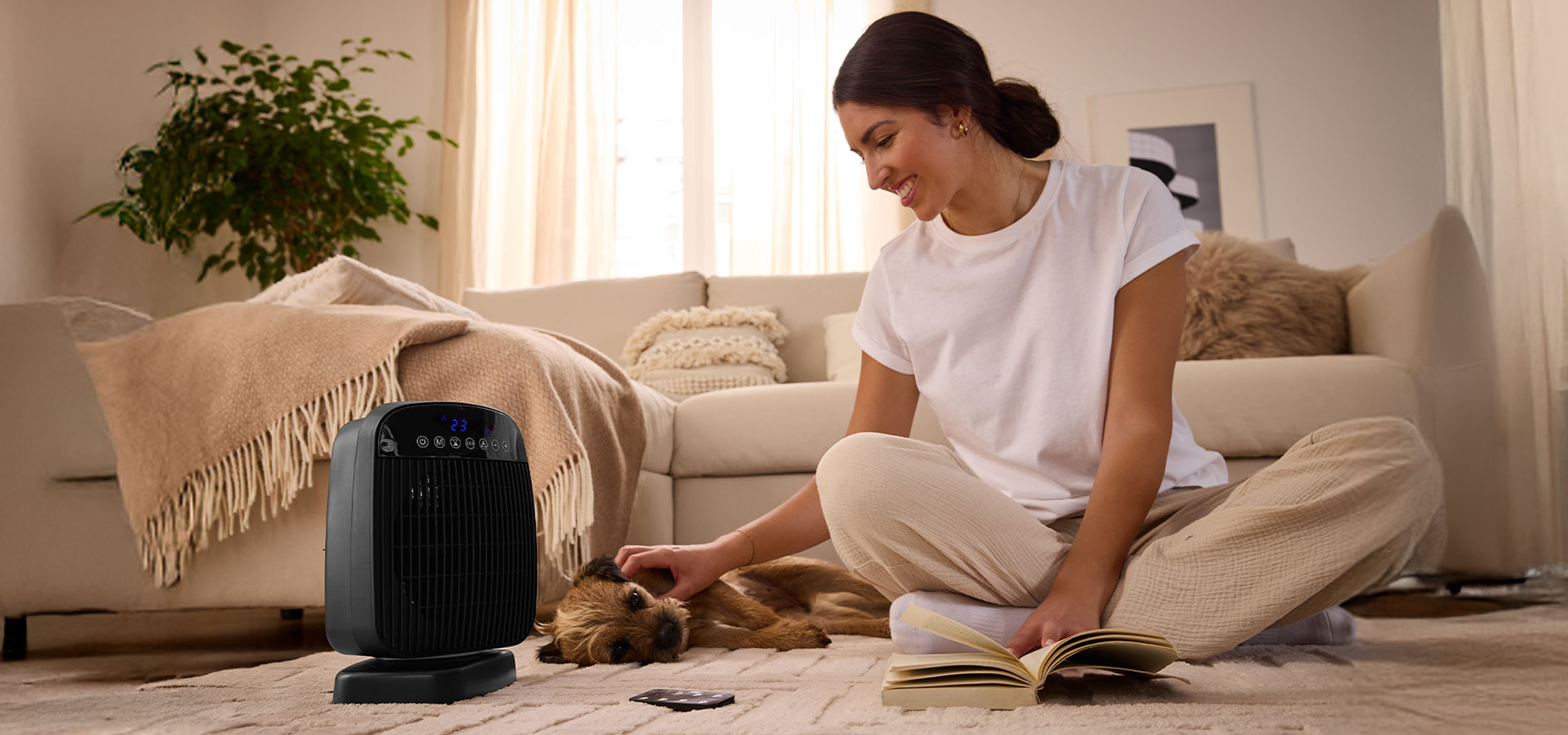 A woman plays with a dog next to an electric heater in a living room.