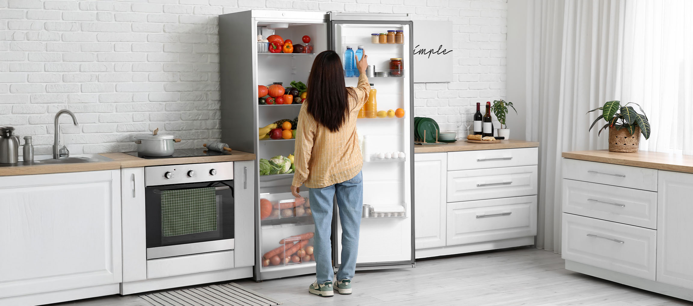 Woman reaching for drinks in a fridge full of fresh produce in a modern kitchen.