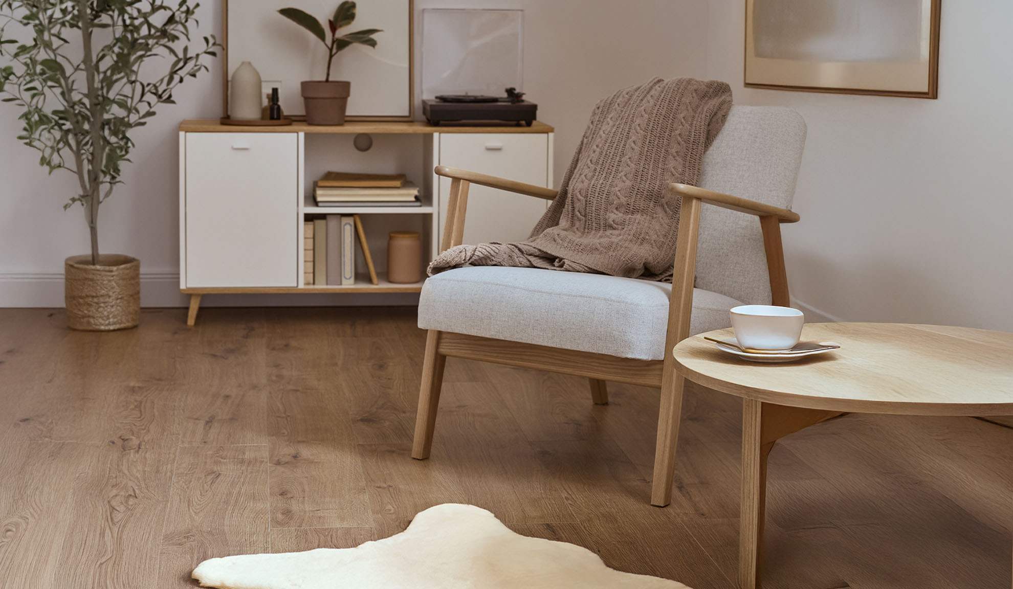 Cozy armchair with throw, wooden coffee table, and storage cabinet in a bright living room.