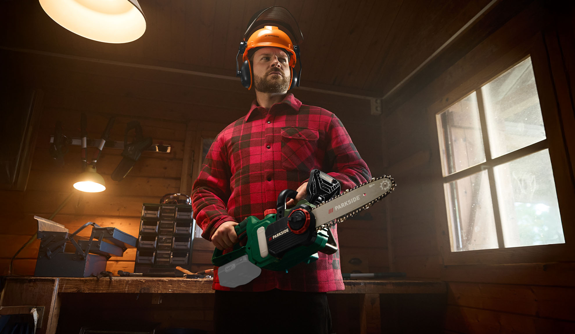 Man in Parkside safety gear and plaid shirt holding a Parkside chainsaw in a workshop