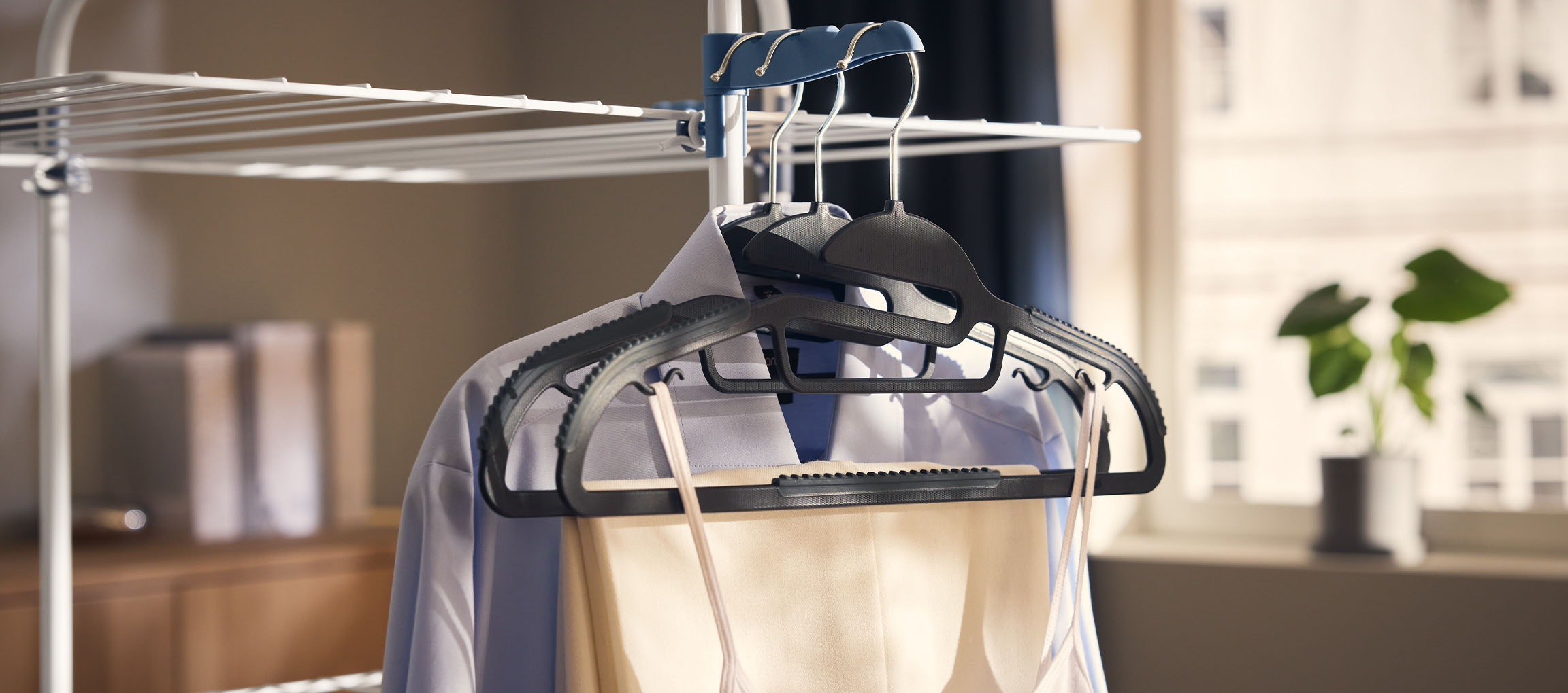 Clothes on hangers on a drying rack, with a plant in the background.
