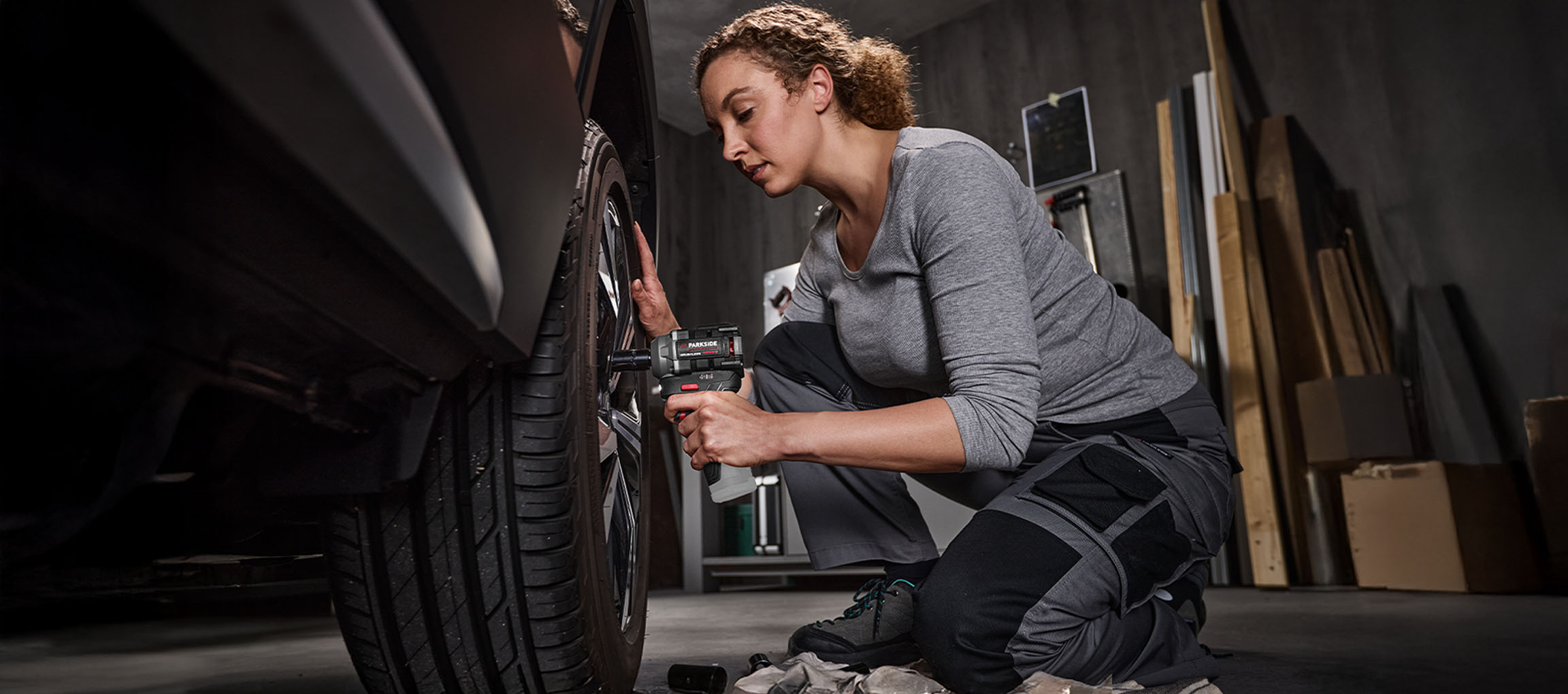 Woman using a Parkside impact wrench to change a car tire in a garage.