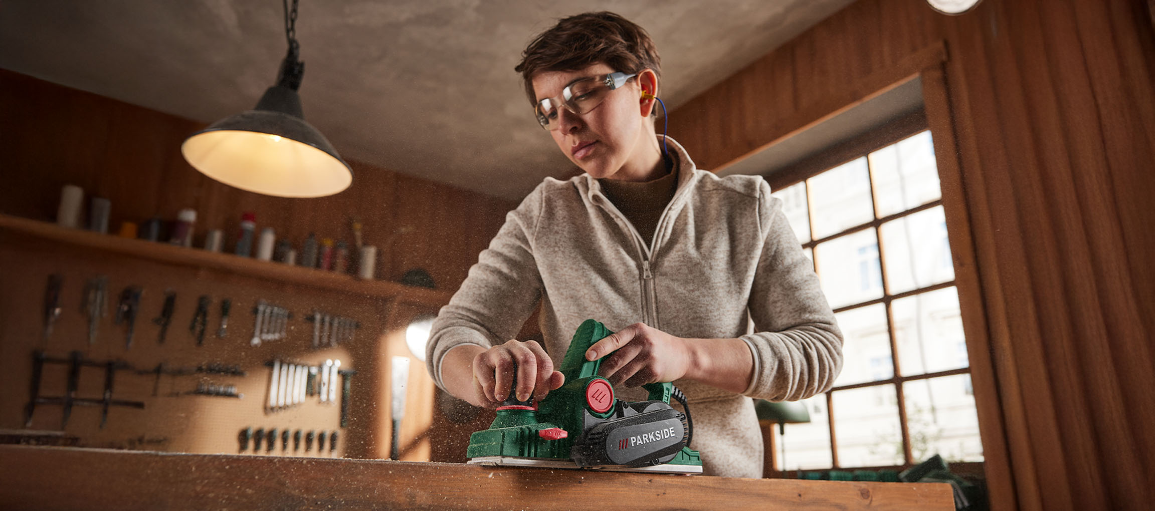 Person using a Parkside electric planer on wood, wearing safety glasses and earplugs.