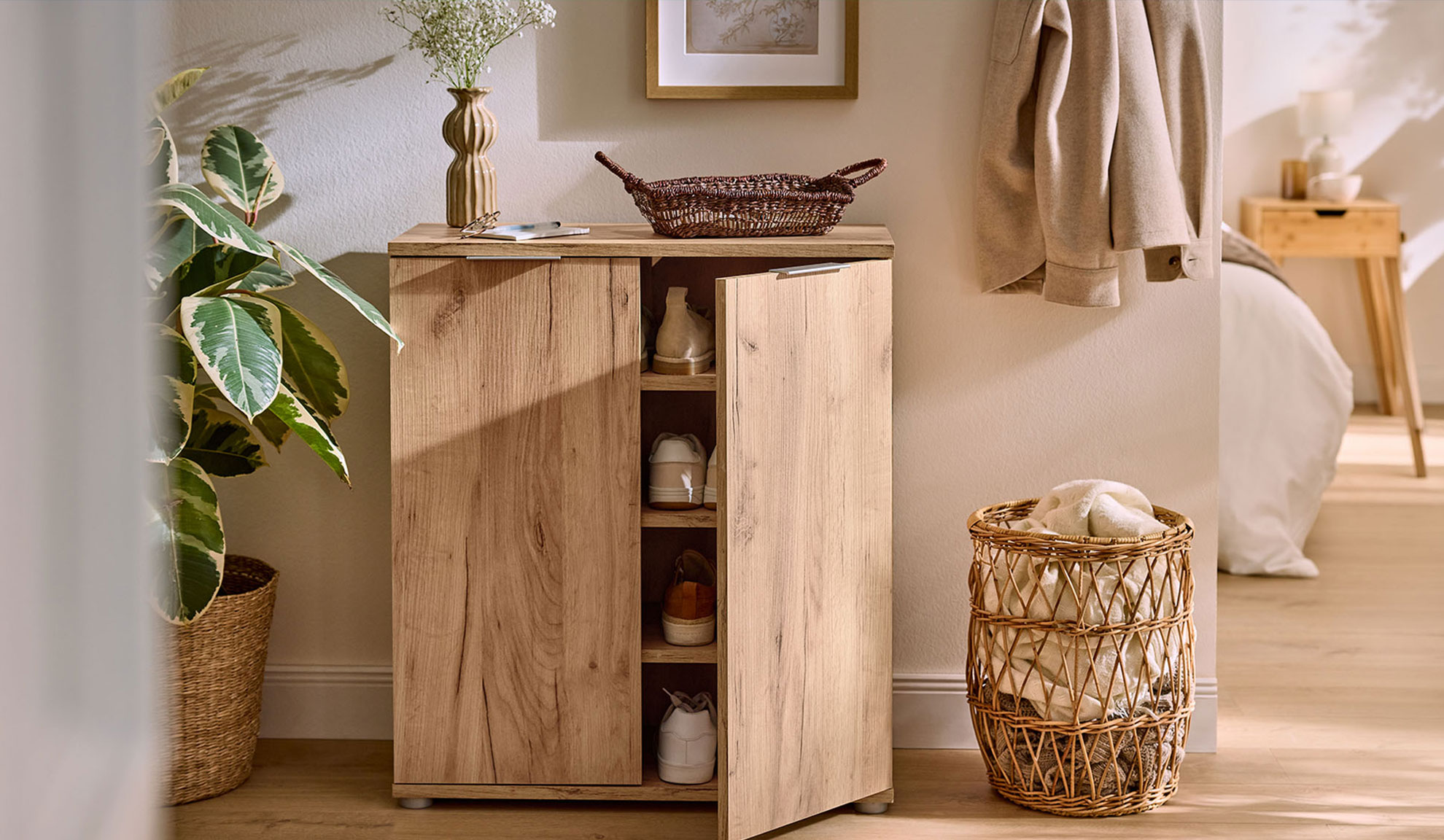 Wooden shoe cabinet with an open door, next to a plant and a basket.