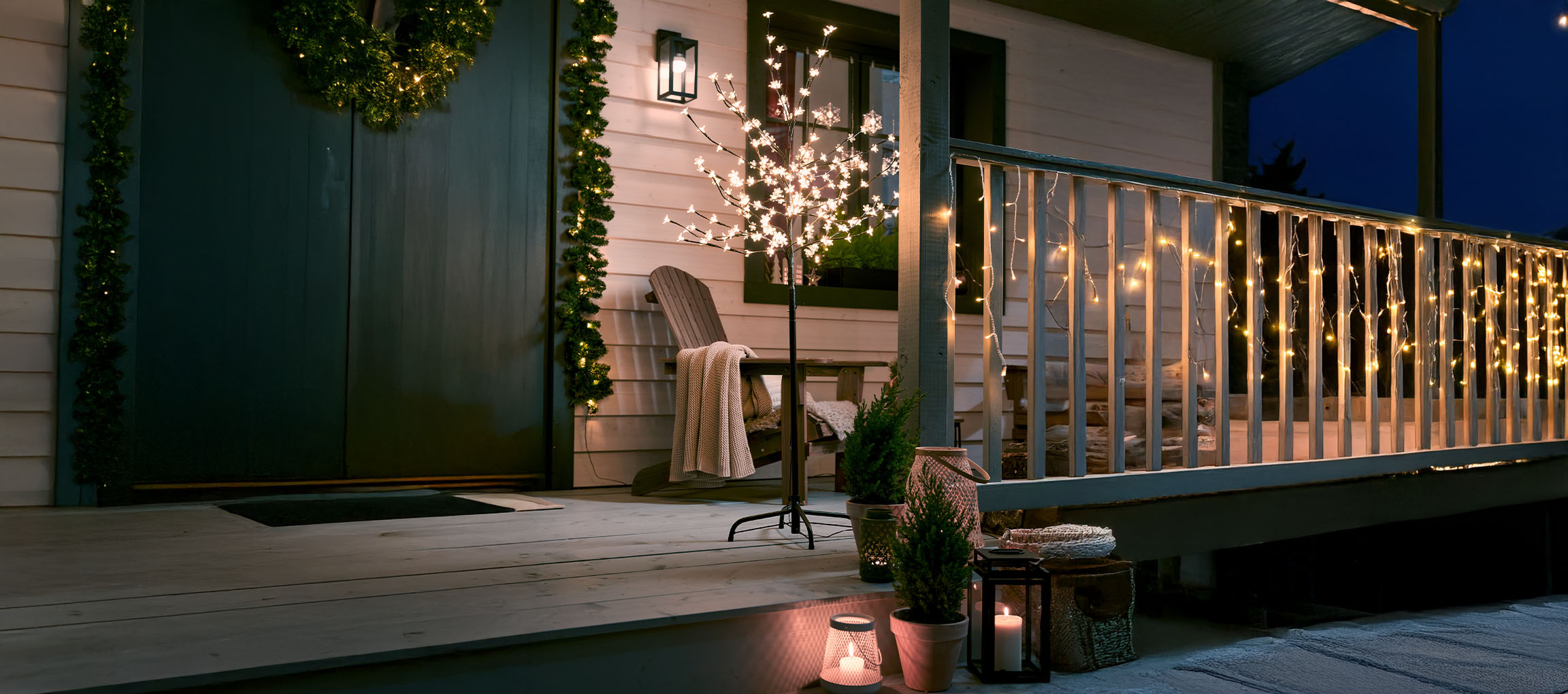 Porch decorated with string lights, a light-up tree, and candles for a festive ambiance.