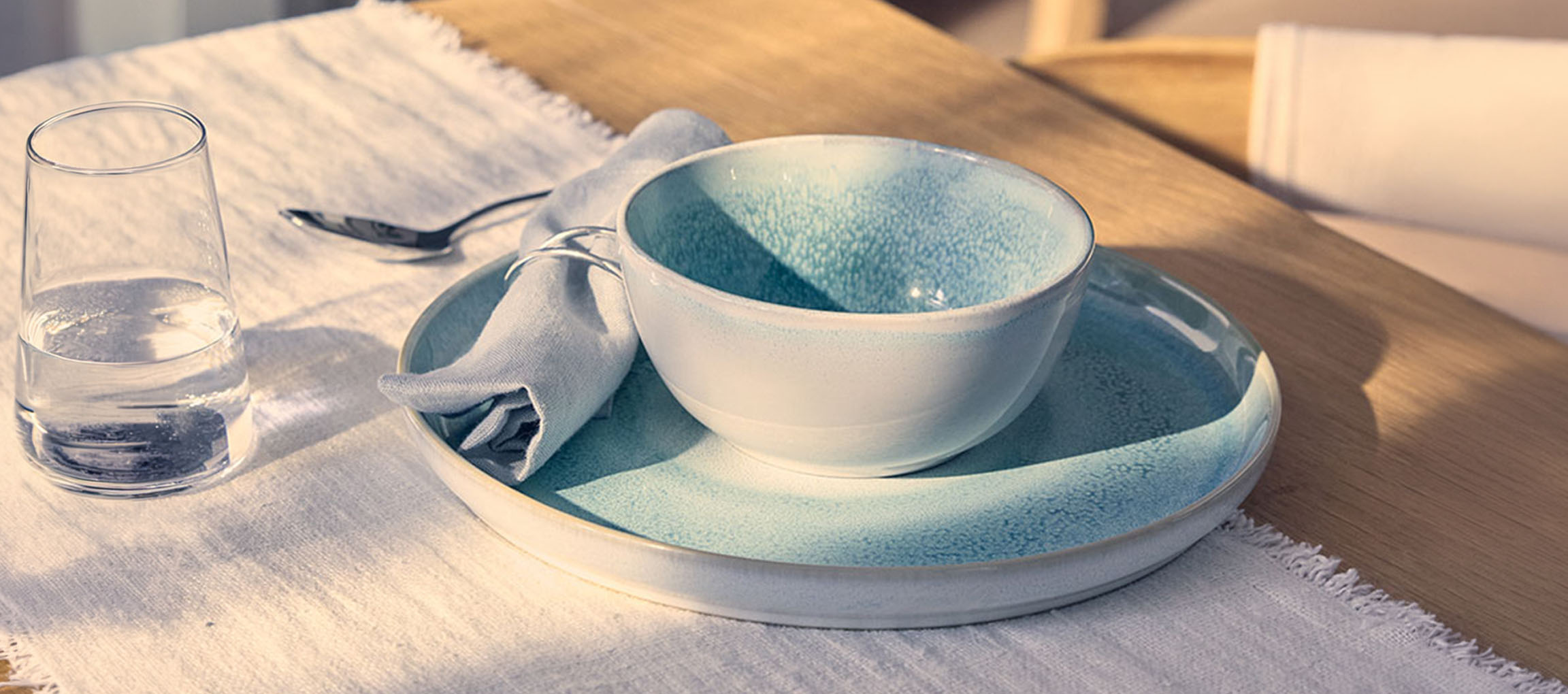 Table setting with a blue ceramic bowl and plate, glass of water, and napkin.
