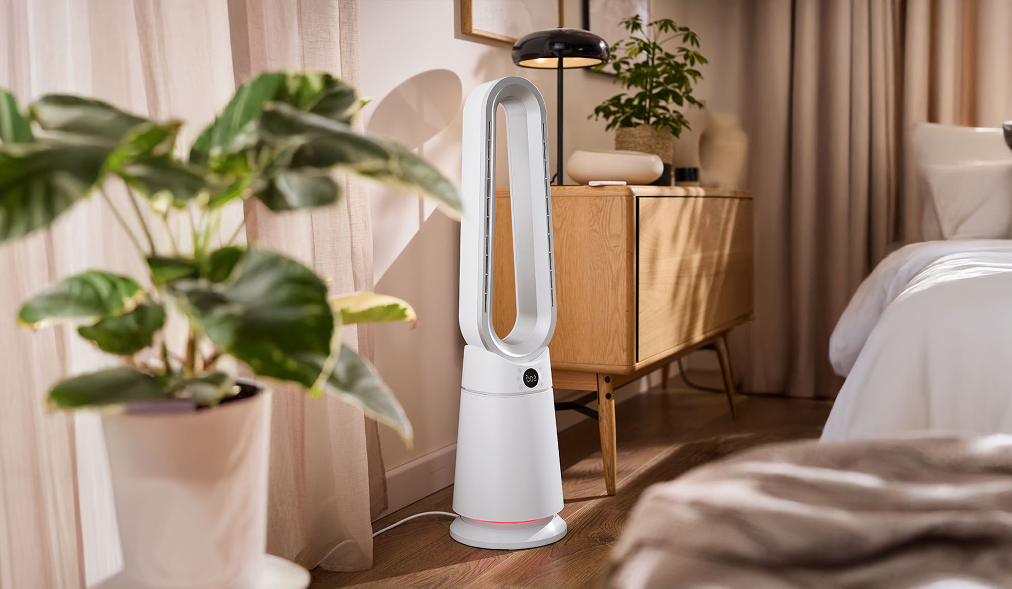 White tower fan in a modern bedroom with plants and wooden furniture.