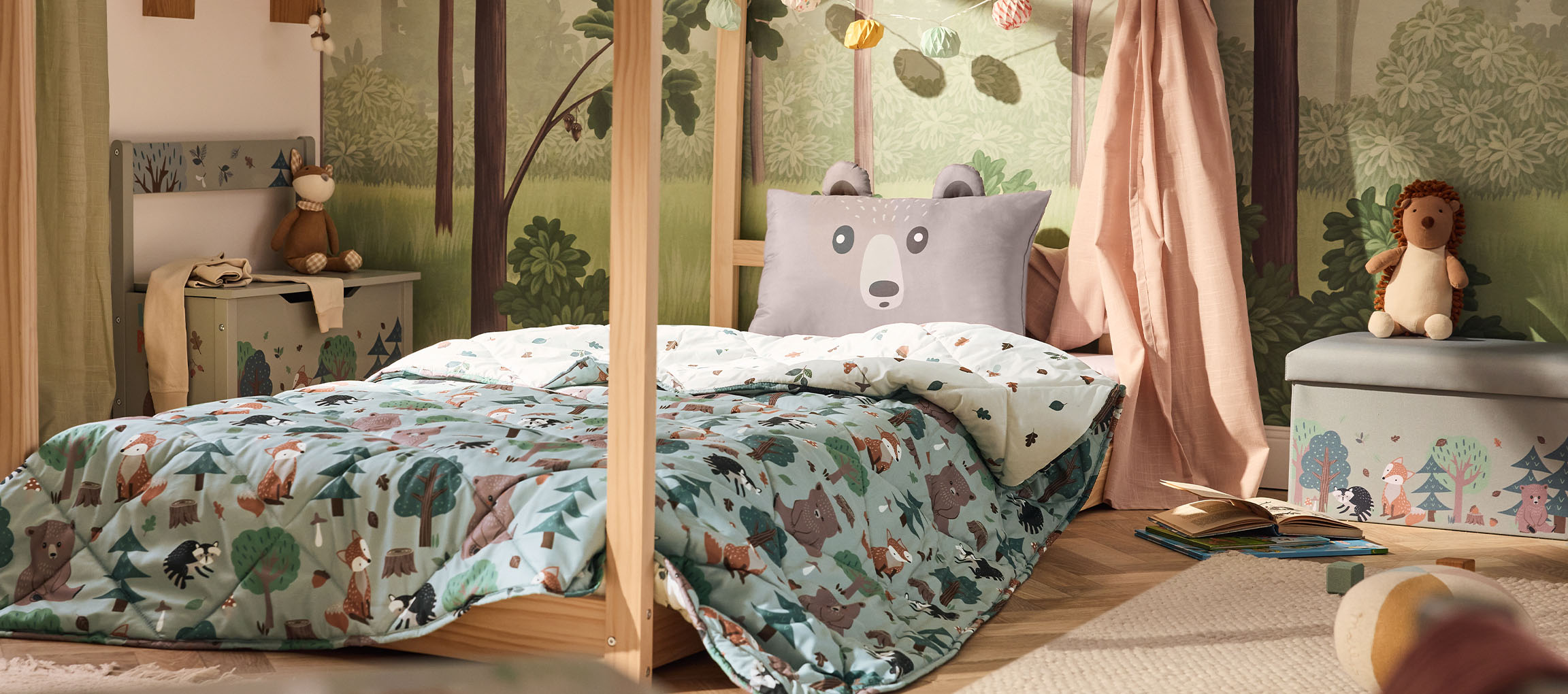 Children's bedroom with wooden bed, bear pillow, and forest-themed duvet.