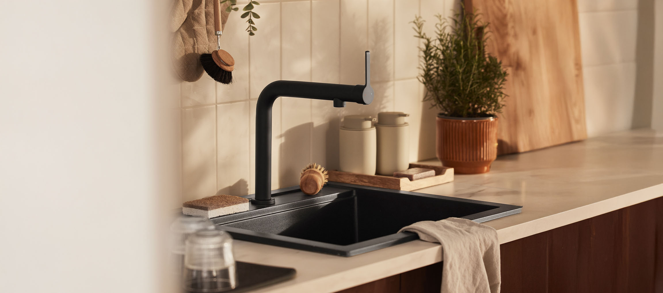 Modern kitchen sink with black faucet, dish brushes, and green plant.