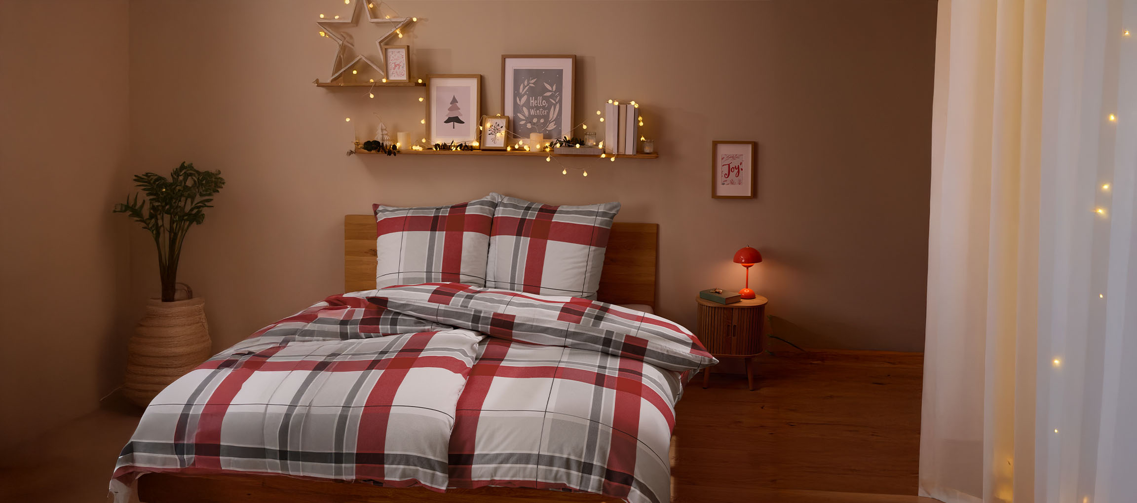 Cozy bedroom with red and grey plaid bedding, Christmas decorations, and string lights.