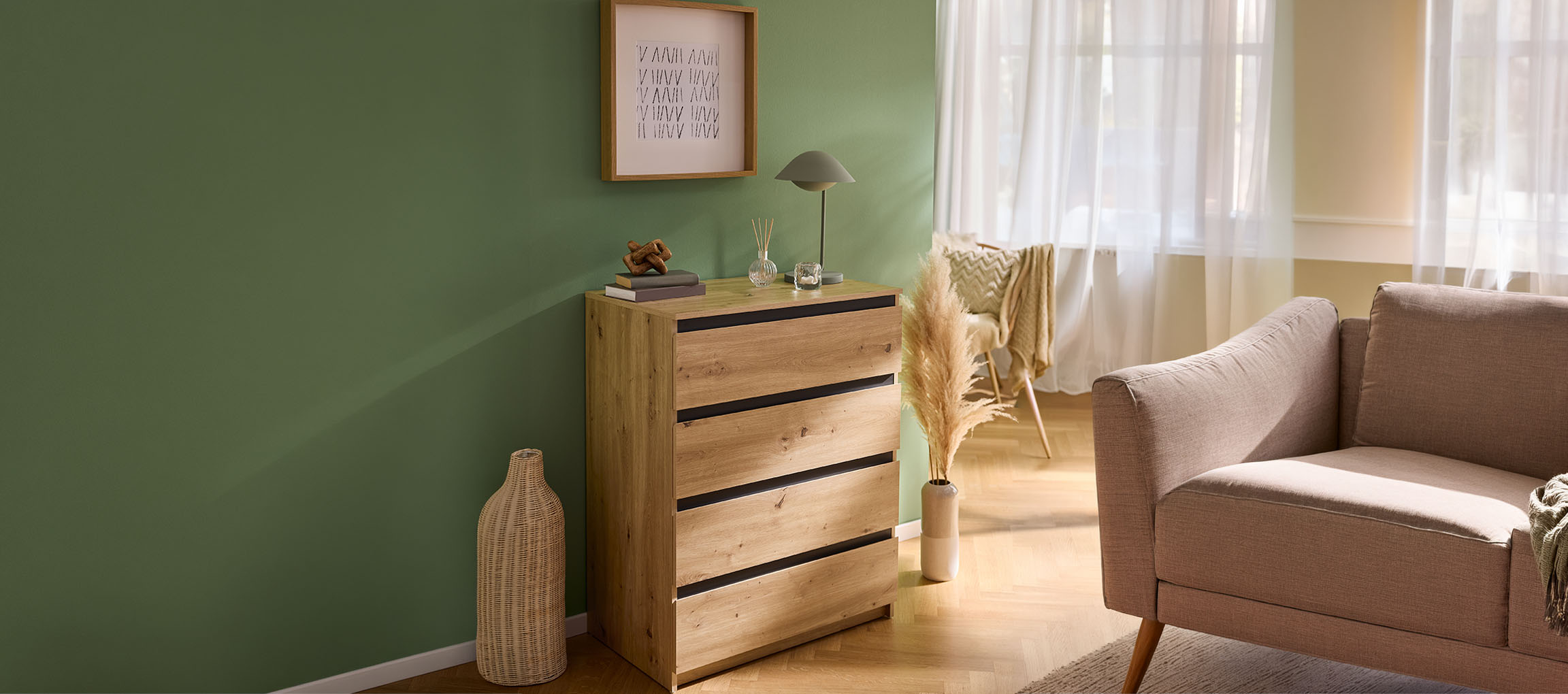 Wooden chest of drawers with black drawers, decorated with a picture and a lamp, in a green living room.
