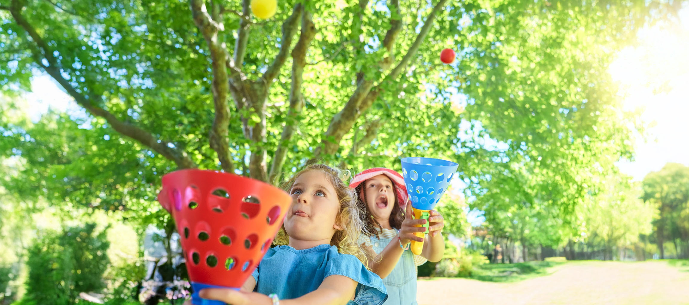 Two girls play a catching game with colorful tossers in a sunny park.