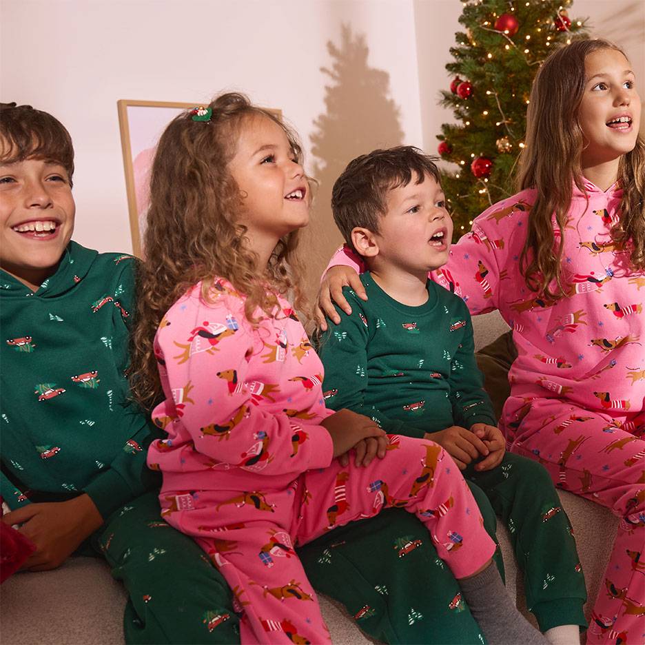 Four children in Christmas pajamas with dog and car patterns, sitting in front of a Christmas tree.