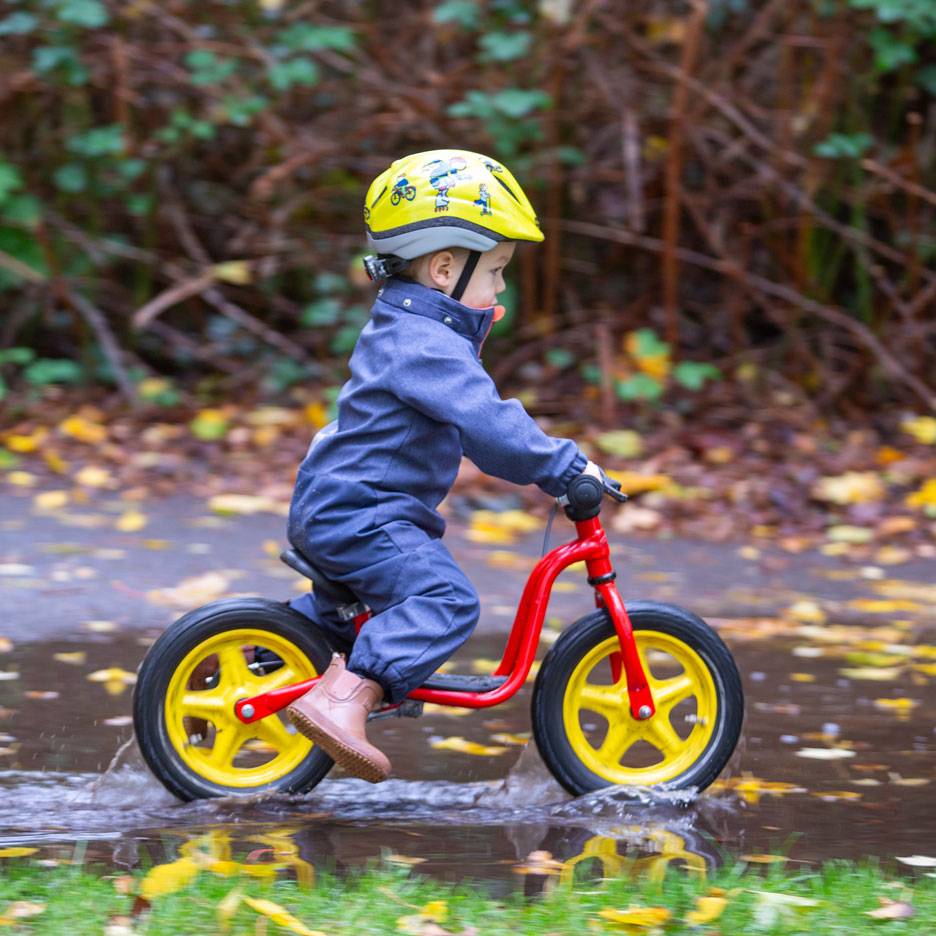 Child on balance bike in a puddle, with helmet and jumpsuit.