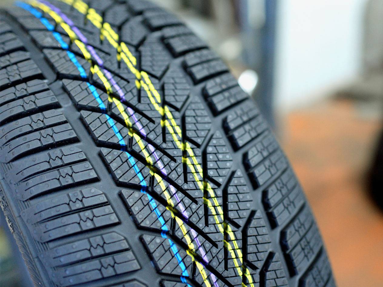 New winter tire with yellow, blue, and purple colored lines on the tread.