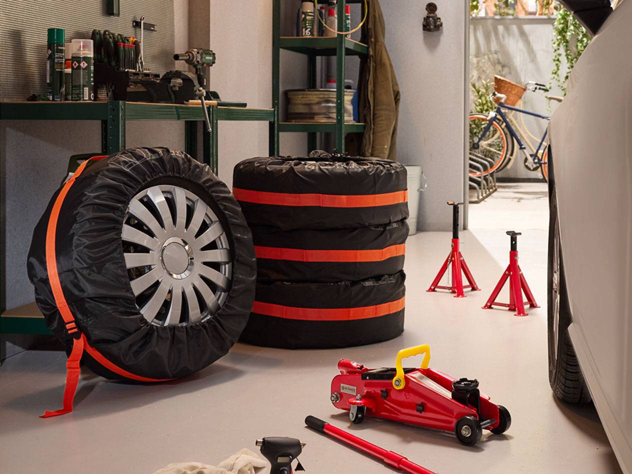 Winter tires packaged with covers, hydraulic jacks, and car stands in a garage.