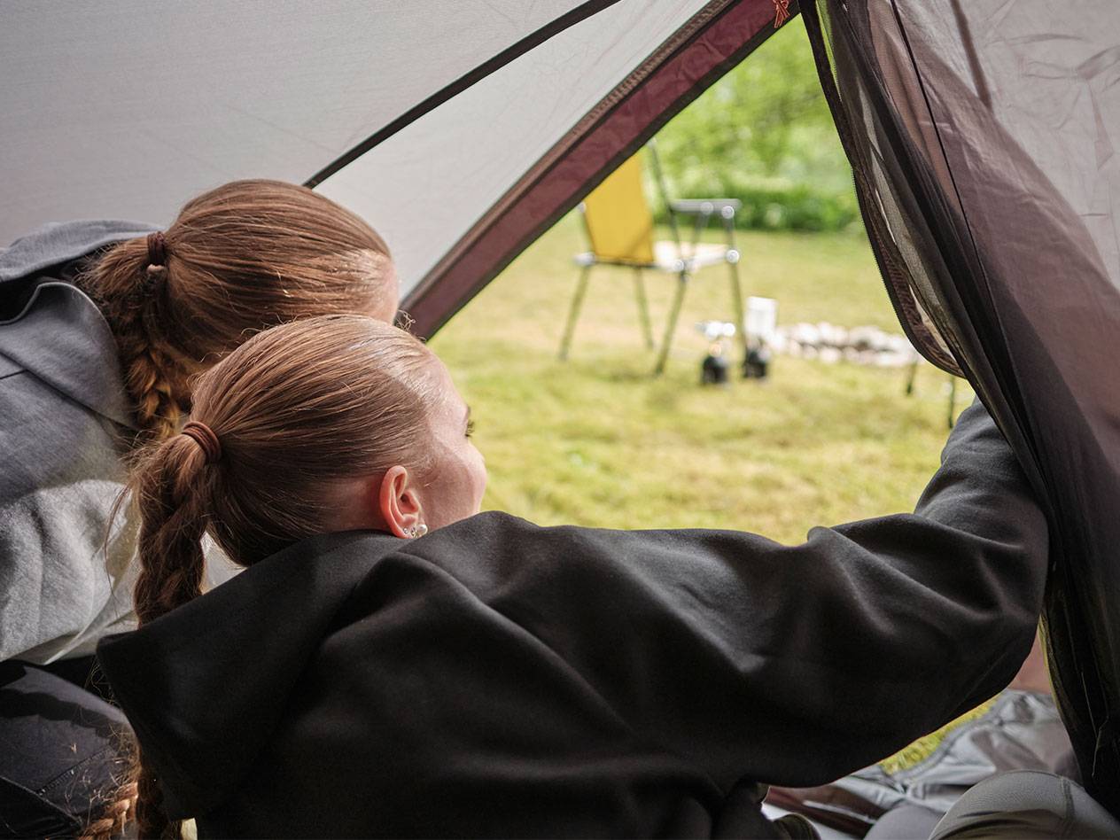 Two girls peek out from a tent opening.
