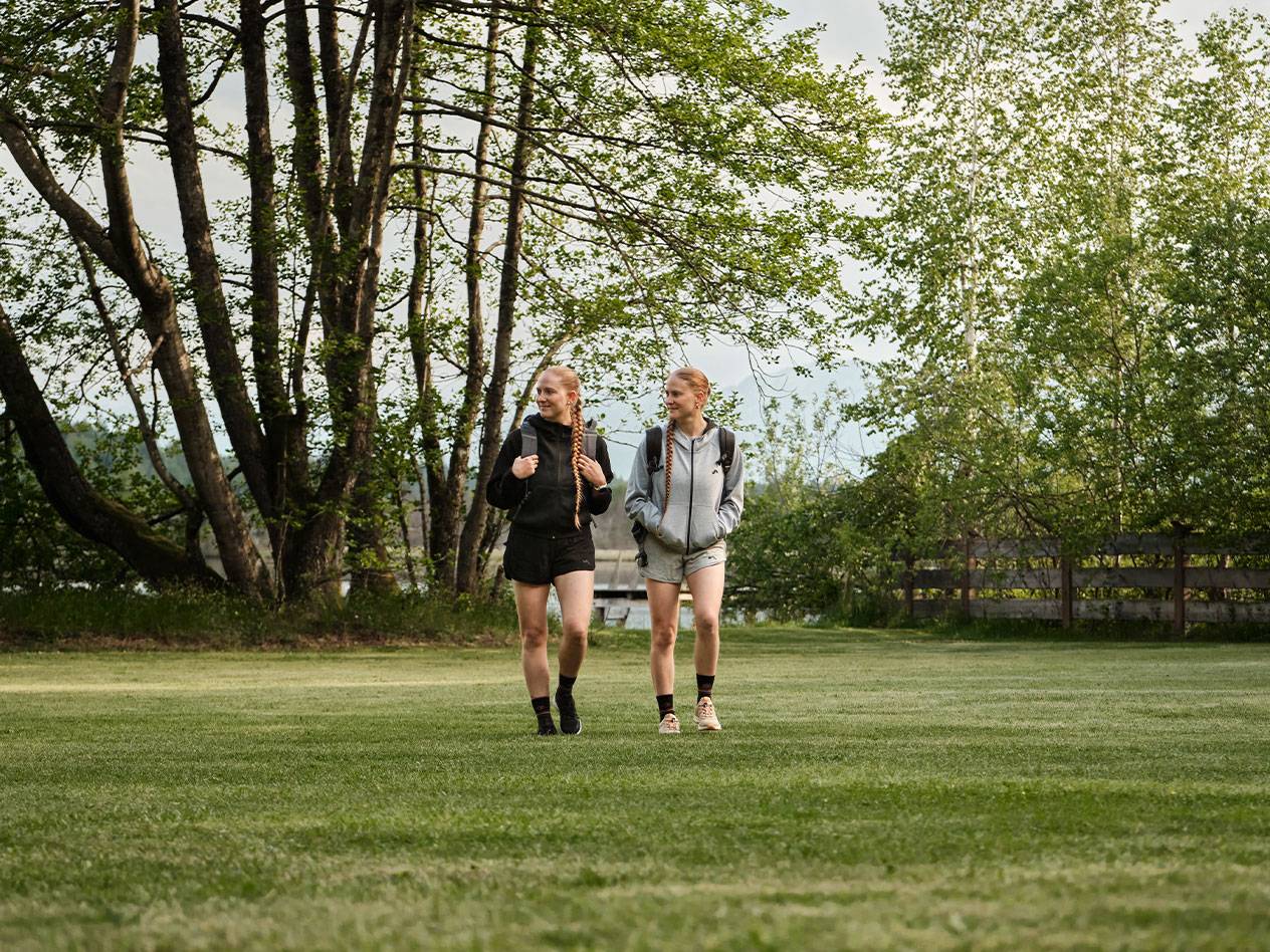 Two girls with backpacks walk across a grassy field.