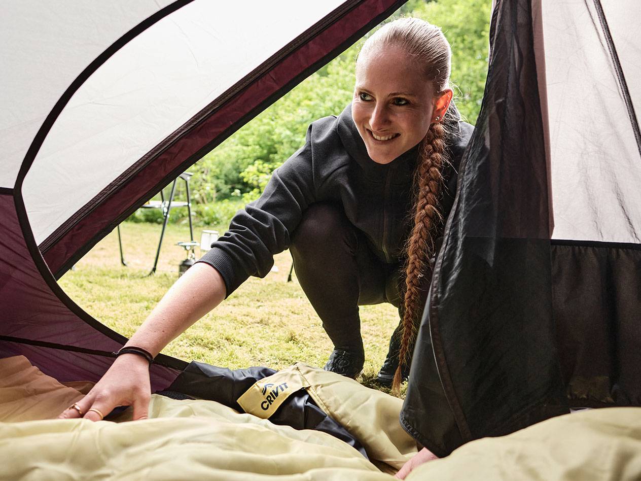 A woman puts a Crivit sleeping bag in a tent.